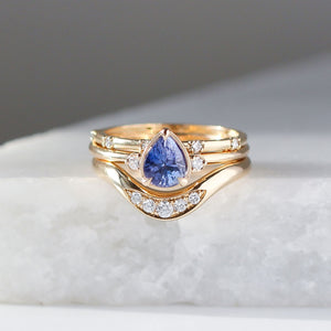 Pear Cut Purple Sapphire ring stacked with diamond gold wave band on marble detail front view