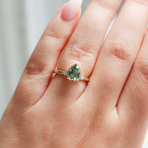 Pear cut green sapphire engagement ring on hand in sunlight